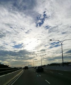 Road passing through highway against cloudy sky