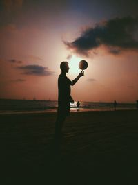 Silhouette man playing with ball at beach against sky during sunset