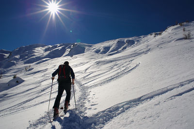 Low angle view of hiker walking on snow covered mountain against bright sky