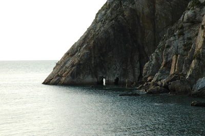 Rock formation by sea against clear sky