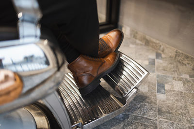 Close-up view of the legs of a man in leather shoes sitting on armchair in a barbershop