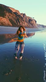 Portrait of young woman standing at beach against clear sky