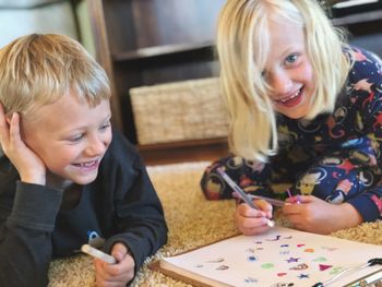 Portrait of smiling girl with brother drawing on paper at home