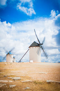 Whitewashed traditional windmills on field against sky