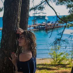 Side view of young woman against tree trunk