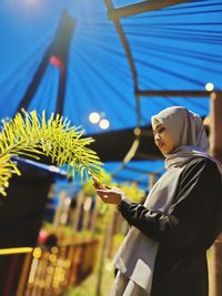 Low angle view of woman in hijab touching plant outdoors