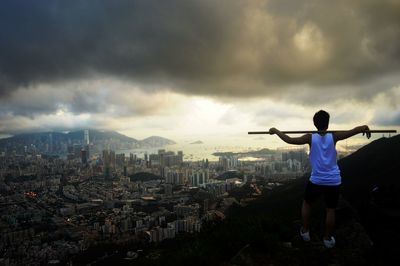 Rear view of man holding stick and standing on cliff against residential district