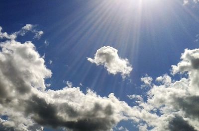 Low angle view of sun shining through clouds