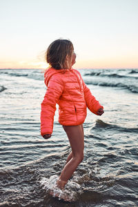 Playful little girl enjoying a free time over sea on a sand beach at sunset during summer vacation