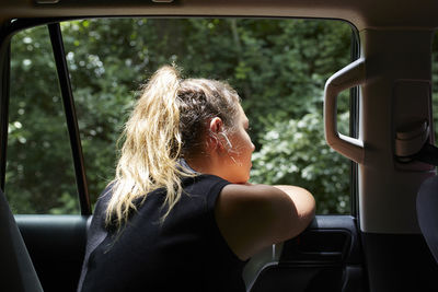 Young blond woman leaning out car window listening music with headphones