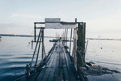 Rear view of man walking on pier amidst lake