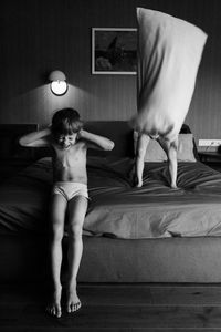 Full length of shirtless young woman standing on bed at home