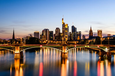 Illuminated bridge over river by buildings against sky in city