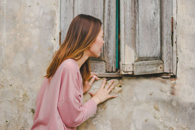 Side view of mid adult woman peeking through wooden window