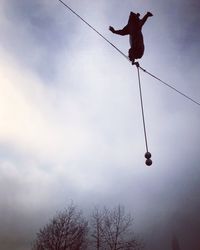 Low angle view of silhouette man hanging on rope against sky