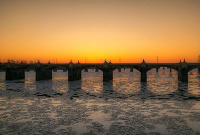 Silhouette bridge over river against sky during sunset