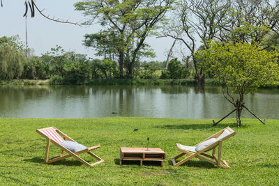 Sunbeds or bed chairs and table on green grass by pond at garden of outdoor cafe and restaurant.