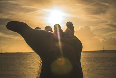 Cropped hand of person over sea against sky