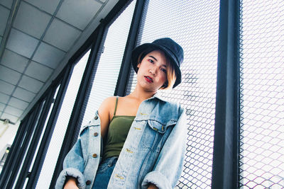 Portrait of beautiful young woman standing against fence