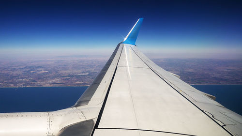 Low angle view of airplane flying over landscape against blue sky