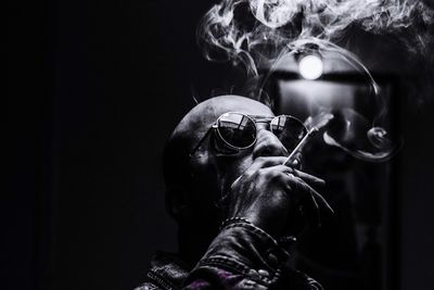 Fashionable man wearing sunglasses smoking cigarette at night