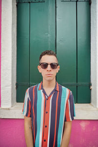 Portrait of man wearing sunglasses standing against wall