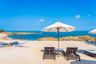 Chairs on beach by sea against blue sky