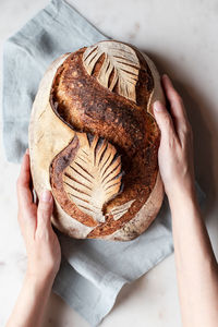 Top view of crop anonymous person with freshly baked bread with creative leaf pattern on white background in light kitchen person