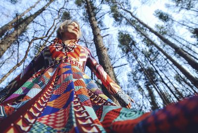 Low angle view of mature woman in dress against tree in forest