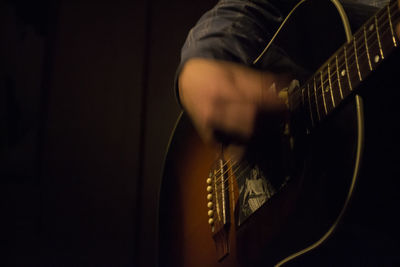 Cropped hand of man playing guitar in darkroom