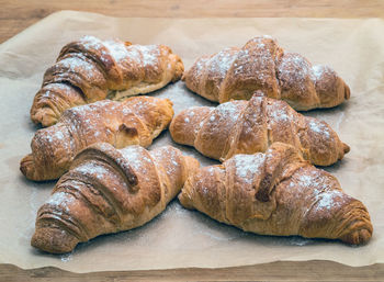 Freshly baked homemade croissants on baking paper sprinkled with powdered sugar.