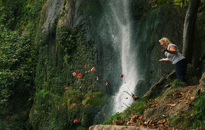 Surprised woman looking at autumn leaves falling by waterfall