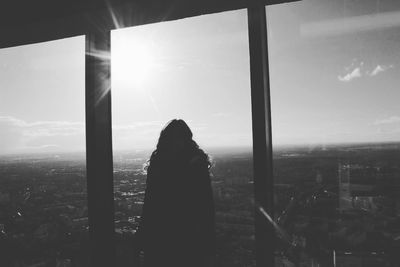 Silhouette woman standing by glass window against cityscape on sunny day