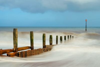 Wooden posts on beach against sky