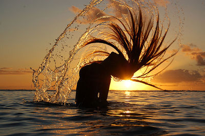 Silhouette of man at sea against sky at sunset