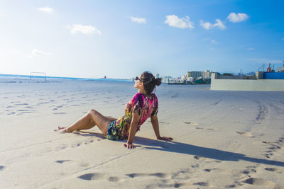 Rear view of woman sitting at beach against sky