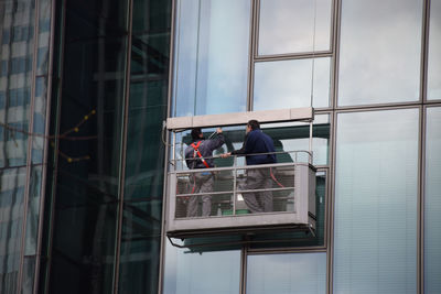 Low angle view of window washers cleaning glass building