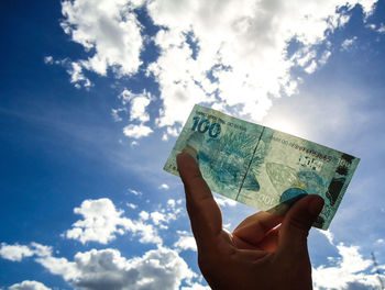 Cropped holding paper currency against sky