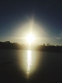 Sun shining over sea against sky during sunset