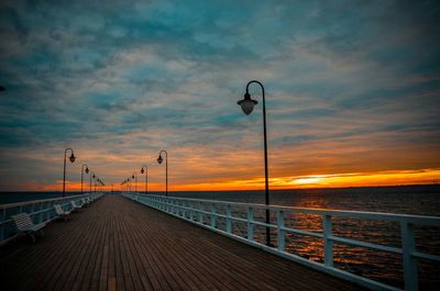 Empty bench and street lights on pier over sea during sunset