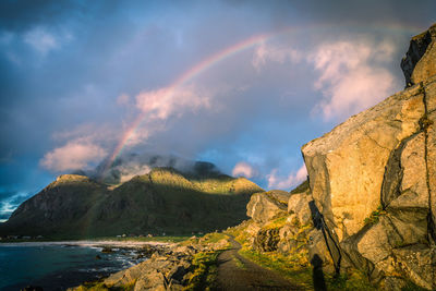 Scenic view of rainbow over mountains, dirt road against sky, lofoten, norway