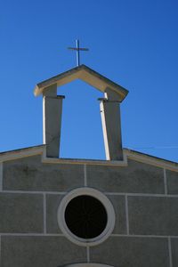 Low angle view of cross on building against clear blue sky