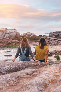 Rear view of women sitting on rocks against sky