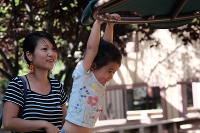 Woman looking at daughter hanging on play equipment at playground