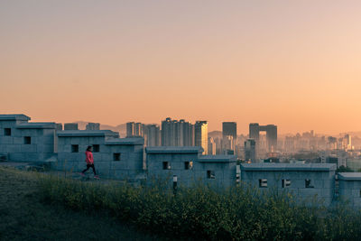 Man by buildings against clear sky during sunset