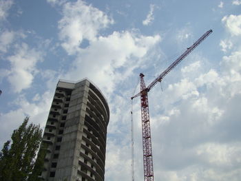 Low angle view of crane by building against sky