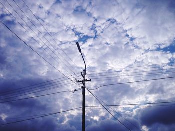 Low angle view of electricity pylon against cloudy sky