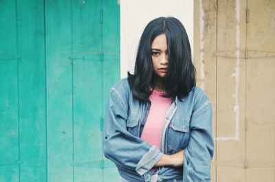 Thoughtful woman wearing denim jacket against wall