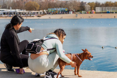 Young girl and her mother on relaxing vacation by the lake with their cute miniature pinscher.