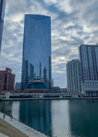 Modern buildings by river against sky in city